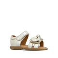 The Clarks Samara Toddlers Gold Leather Sandal in D Narrow Width features a gold leather finish, decorative bow on the front strap, ankle velcro closure, open toe, and brown sole—ideal for girls needing narrow sandals. Displayed on a white background.