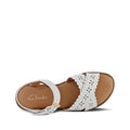 The Clarks Girls Hallie White Sandals (E width) feature decorative cutout patterns on two crossing straps with buckle fastening, a tan footbed, and the Clarks logo on the insole, all shown displayed on a plain background., 9336078590978, 9336078590992, 9336078591012, 9336078591036, 9336078591050, 9336078591074, 9336078591098, 9336078591111, 9336078591135