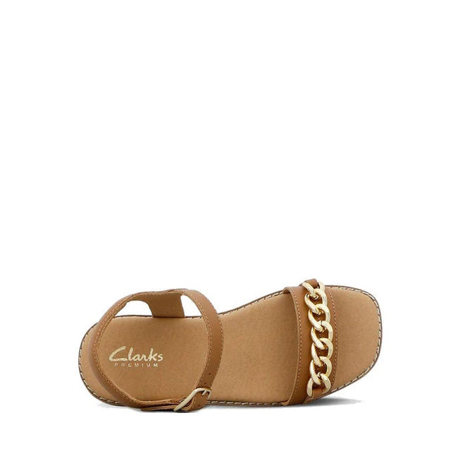 The Clarks Girls Amy Tan Leather Sandal Special Occasion features an adjustable ankle strap and a bold gold chain across the toe. Displayed on a white background, these stylish leather sandals are perfect for any fashionable girl., 40498, 40499, 40500, 40501, 40502, 40503, 9336078207838, 9336078207852, 9336078207876, 9336078207890, 9336078207913, 9336078207937, 9336078207951, 9336078207975, 9336078207999, 9336078208019, 40514, 40515