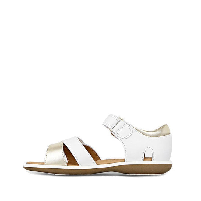 The Clarks Girls Pippa White Leather Sandals (E width) feature a white and gold leather upper, open toe, adjustable hook-and-loop ankle strap, and flat brown sole, shown in profile on a white background., 9336078233325, 9336078233349, 9336078233363, 9336078233387, 9336078233400, 9336078233424, 39947, 39948, 9336078233066, 9336078233080, 9336078233103, 9336078233127, 9336078233141, 9336078233165, 39939, 39940