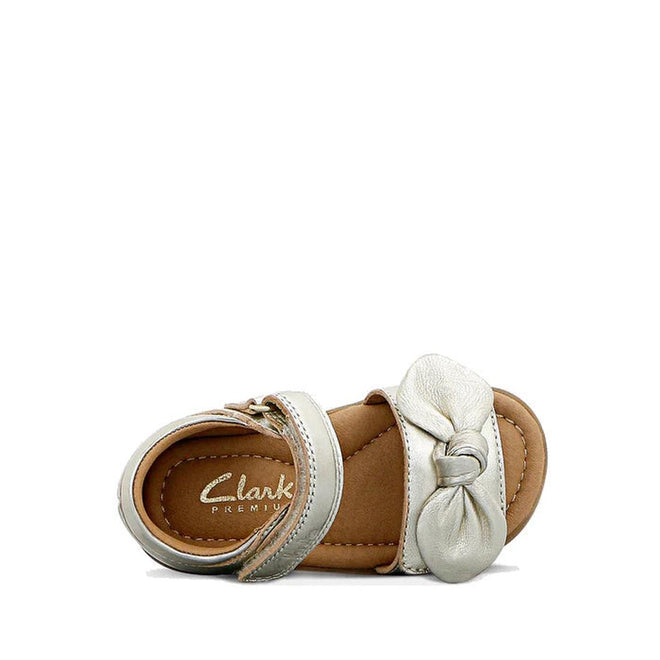 The Clarks Samara Toddlers Gold Leather Sandal (D Narrow Width) features a metallic gold leather upper, knotted bow on the front strap, Velcro ankle strap, branded “Clarks Premium” insole, and tan sole. Displayed on a white background., 40541, 9336078235183, 9336078235220, 9336078235268, 9336078235305, 40546, 40547, 40548, 40549, 40532, 9336078234926, 9336078234940, 9336078234964, 9336078234988, 9336078235008, 9336078235022, 9336078235046, 9336078235060