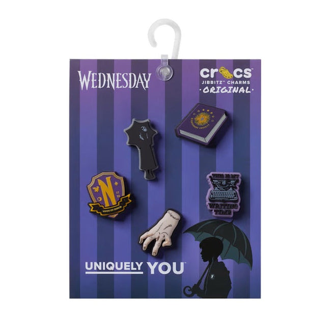 The Crocs Jibbitz 5 Pack - Adams Family features five Wednesday-inspired charms—a dress, book, crest, hand, and silhouette with umbrella—on a purple striped "Wednesday Uniquely You" card. Perfect for fans—get yours at a discount!.