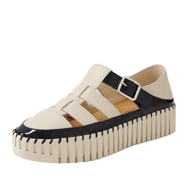 A pair of Django & Juliette Baytown Black Almond Patent Leather Flats featuring a cream and black fisherman-style design, complete with a chunky ribbed cream sole, open side cutouts, and a black buckle strap over the instep.