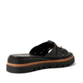 The Django & Juliette Scoop Platform Slide Black features thick crossed black leather straps, a chunky black sole with a brown accent stripe above it, and is shown from the back and side—these chic platform slides effortlessly combine comfort and style for any occasion.