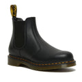 The right foot of a Dr Martens black leather 2976 Chelsea boot with elastic side panels and a pull tab featuring yellow branding. In Nappa a sfter and not too shiny leather. The boot has a sturdy sole with yellow stitching along the edge, giving it a signature look. The background is white.