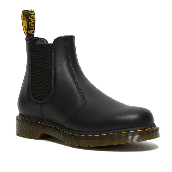 The right foot of a Dr Martens black leather 2976 Chelsea boot with elastic side panels and a pull tab featuring yellow branding. In Nappa a sfter and not too shiny leather. The boot has a sturdy sole with yellow stitching along the edge, giving it a signature look. The background is white.