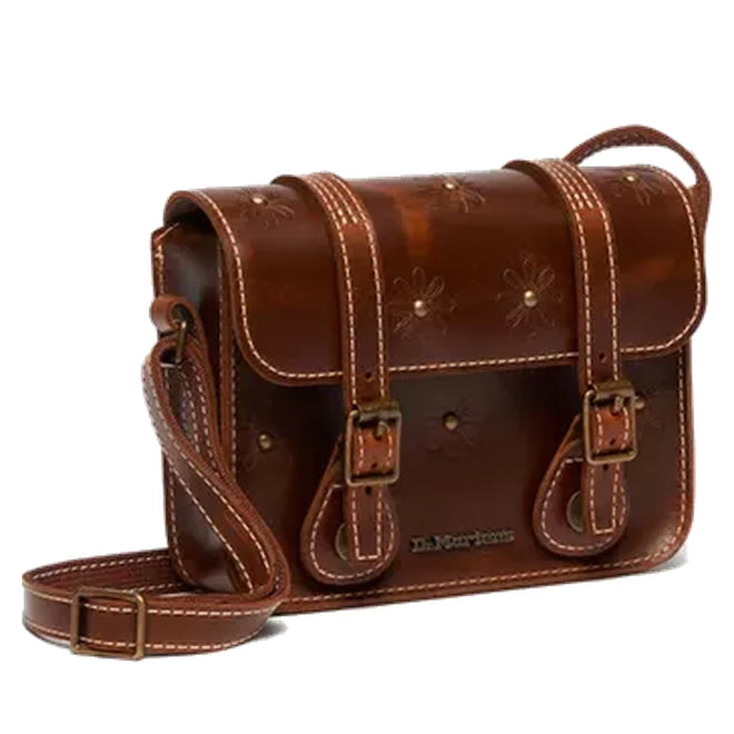 The Dr Martens Leather Cross Body Amber Tan Leather Satchel 7 inch features white stitching, two buckled front straps, a long adjustable shoulder strap, and embossed flower designs on the flap and front.