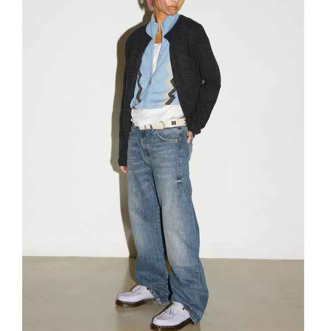 A person stands against a white wall wearing a black jacket, blue zigzag shirt, baggy blue jeans, a white belt, and Dr Martens Adrian Lavender Frost Virginia Leather Tassel Loafers. Their face is partially out of frame., 41118, 190665677430, 190665677447, 190665677454, 190665677478, 41124, 41125, 41126, 41127, 41128