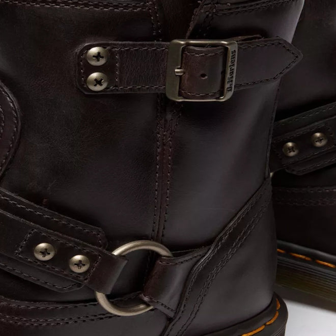 Close-up of Dr Martens Anistone Harness Bex Crazy Dark Brown Horse Biker Boots with a slightly glossy, textured leather, metal buckles, rivets, circular ring detail, and orange stitching accenting the sole., 49399, 190665745689, 190665745696, 190665745719, 49407, 49409, 49411, 49412