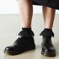 A person wears Dr Martens Ankle Frill Cotton Blend Socks in black and black leather lace-up shoes, standing on a light-colored floor with the lower part of a black skirt visible., 190665640809, 190665640793