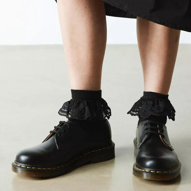 A person wears Dr Martens Ankle Frill Cotton Blend Socks in black and black leather lace-up shoes, standing on a light-colored floor with the lower part of a black skirt visible., 190665640809, 190665640793