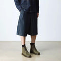 A person wearing a pinstriped jacket, dark knee-length denim shorts, black socks, and Dr. Martens Brookline Chukka Boots in Olive Milled Nubuck Leather with a lightweight outsole stands on a light-colored floor against a plain white background., 51342, 190665797053, 190665797060, 190665797084, 190665797091, 190665797107, 190665797121, 51349