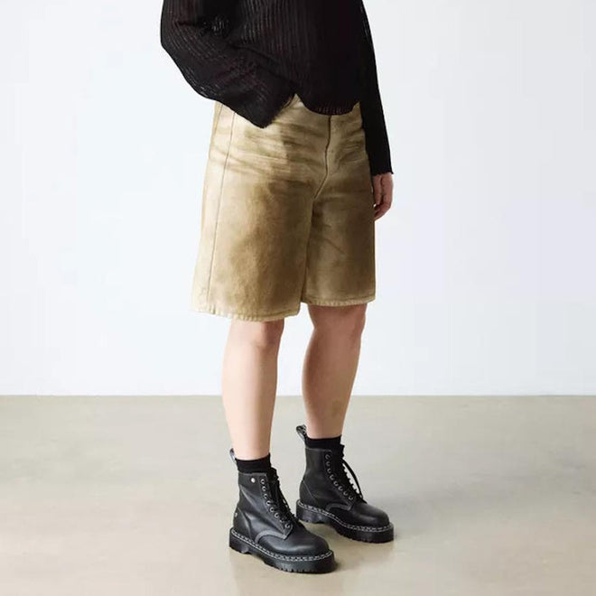 A person wears a black long-sleeve top, tan knee-length shorts, black socks, and Dr Martens Bex 1460 WDS White Stitching Black Boot Sendal, standing against a plain light-colored background., 50363, 50364, 190665803068, 190665803075, 190665803099, 50369, 50370