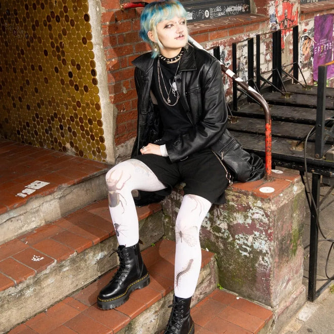 A person with short blue hair sits on outdoor steps, wearing a black leather jacket, black shorts, white tights with insect designs, layered necklaces, and Dr Martens - Jadon Polished Smooth Boot 8 up; graffiti and yellow tiles are in the background., 883985578883, 883985578890, 883985578906, 883985578913, 883985578920, 883985578937, 883985578944, 883985578951, 883985578975, 883985578968