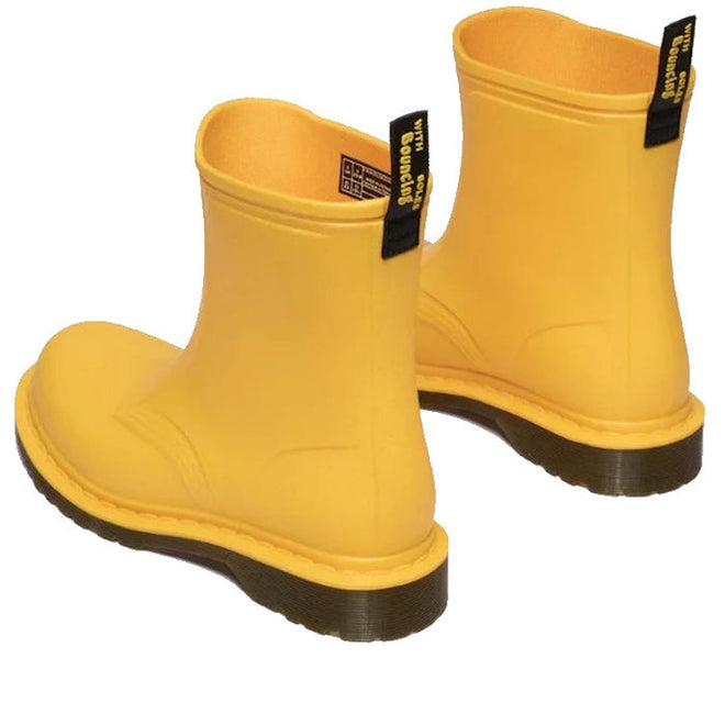 A pair of Dr Martens 1460 Sub Max Pull On Rain Boot Yellow PVC with black pull tabs and thick dark brown soles, styled with one boot forward and one angled—ideal as a stylish waterproof choice for wet days., 49435, 190665746464, 190665746471, 190665746495, 49440, 49441, 49442