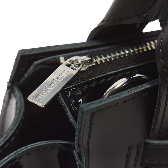 Close-up of the Dr Martens Small Keiv Leather Tote Bag in black, featuring a shiny patent leather surface and detailed stitching. The silver zipper pull, engraved with Dr. Martens, is visible, while sleek patent Lamper straps enhance the bag’s modern aesthetic.