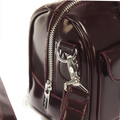 Close-up of the Dr Martens Top Handle Bag in Cherry Red Oxford Rub Off, featuring glossy burgundy leather with silver hardware, including a zipper, detailed stitching, and a metal clasp on the strap—an elegant accessory showcasing the signature oxford rub off finish.