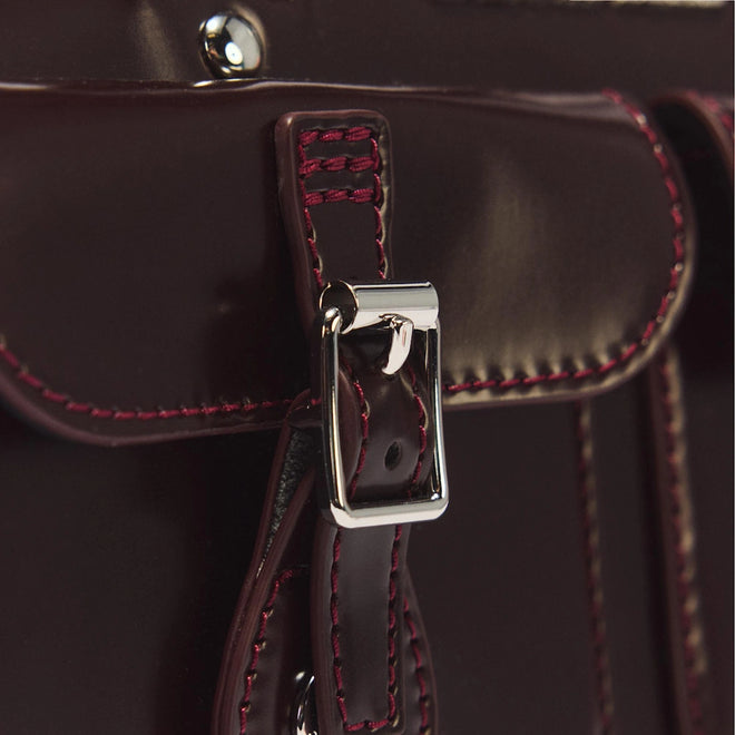Close-up of the Dr Martens Top Handle Bag in Cherry Red Oxford Rub Off leather, featuring a shiny silver buckle and maroon stitching, showcasing detailed craftsmanship and the rich texture inspired by the classic oxford rub off finish.