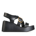 Introducing the EOS Arianis Black Womens Leather Platform Wedge Sandals: these stylish sandals feature a chunky platform wedge sole, crisscross black leather straps, and an adjustable ankle strap accented with a gold buckle. Designed with an anatomical footbed for superior comfort, the EOS Arianis is shown in side profile against a white background., 54247, 9321190083316, 9321190083323, 9321190083330, 9321190083347, 9321190083354, 54253