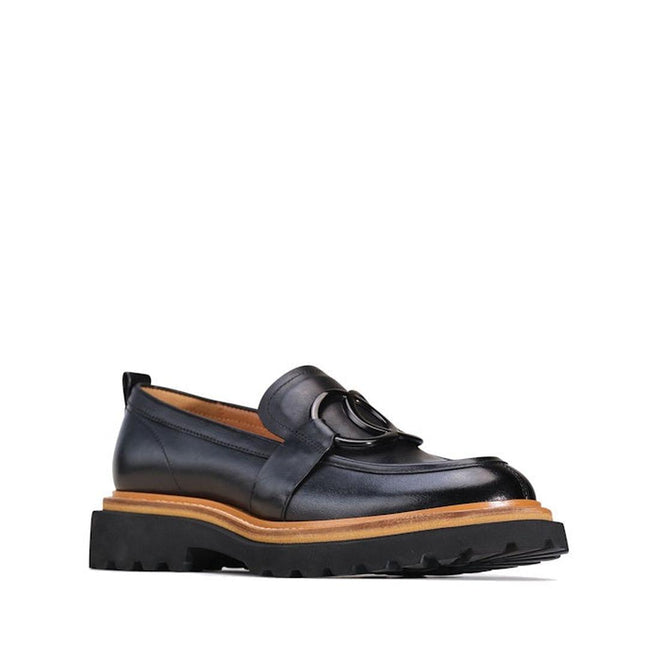 The right foot side & front shot of the Abbi EOS black leather slip-on loafer with a dual round metal ornament vamp and a cleated sole and an tan accent wrapped around the foot seperating teh upper and the sole.