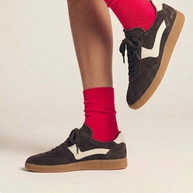 A person wearing Gelato Staton Chocolate Brown / Swan Leather Lace Womens Sneakers with bright red socks stands on one foot, the other slightly raised, set against a neutral background., 52477, 52478, 52479, 52480, 52481, 52482