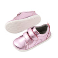 A pair of Bobux Iwalk Toddlers Grass Court Pink Metallic Leather Trainers, featuring shiny pink leather, white soles, and two Velcro straps, shown from both a side and bottom view—perfect trainers inspired by the classic Grass Court style.