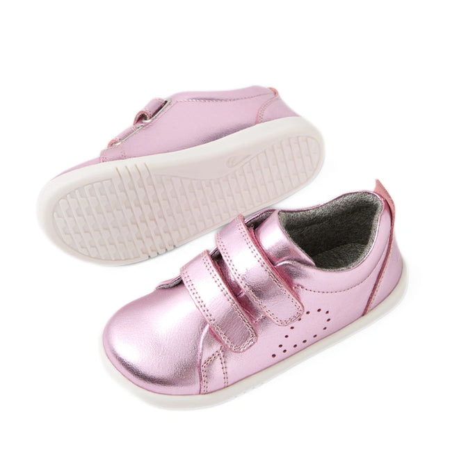 A pair of Bobux Iwalk Toddlers Grass Court Pink Metallic Leather Trainers, featuring shiny pink leather, white soles, and two Velcro straps, shown from both a side and bottom view—perfect trainers inspired by the classic Grass Court style.