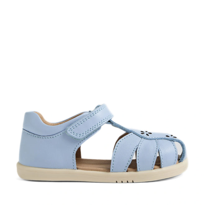 Introducing the Bobux IWalk Holly Toddlers Sandal in Skyway Blue—a light blue children’s sandal featuring a closed heel, open toe, and adjustable Velcro strap. Designed for comfort, these leather sandals have a soft sole and delightful flower-shaped cutouts on the top, making them both practical and charming for little ones. Shown against a white background.
