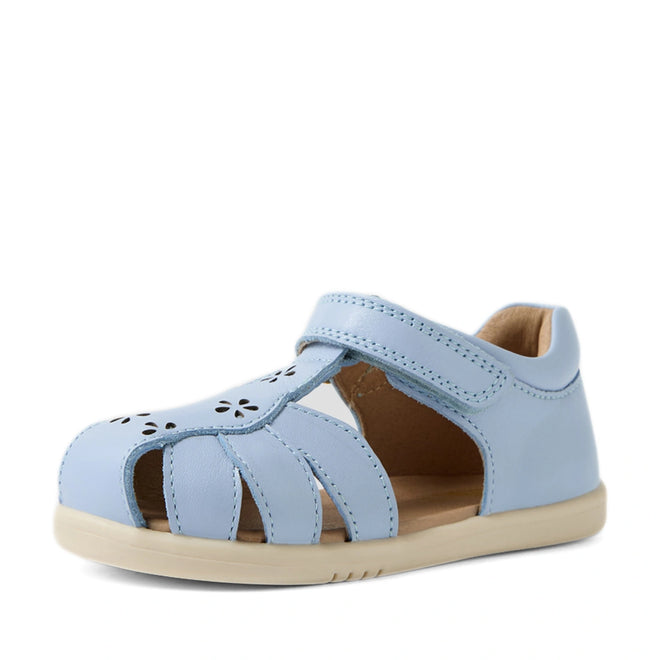 The Bobux IWalk Holly Toddlers Sandal in Skyway Blue features a light blue, closed toe design crafted from quick-drying leather, with delightful floral cutouts on the front. Designed for toddlers, these sandals include side cut-outs and a convenient velcro strap, plus a comfortable flat beige sole.