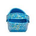 The Crocs Kids – Toddlers Classic Clog K Paint Splatter Print in blue, pink, and multi has a colorful splatter design, textured sole, and pivoting heel strap, shown from the back., 47582, 198445214134, 198445214141, 198445214158, 198445214097