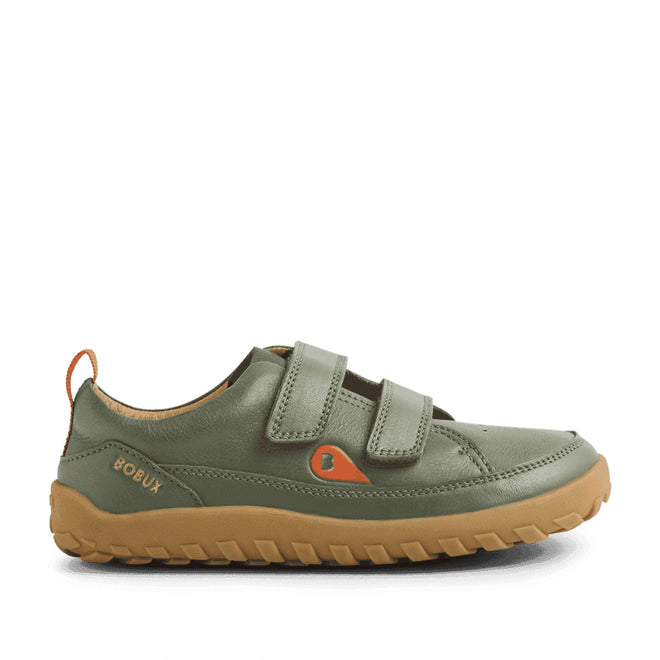 The Bobux KP Kids Plus Dawn Leather Sneaker in Vetiver Green is a child’s shoe crafted from green leather, featuring two Velcro straps, a brown rubber sole, and orange accents such as the pull tab and logo. Designed to support natural foot movement with its wide toe box, these barefoot kids sneakers are displayed in a side view against a white background.