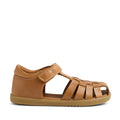 Introducing the Bobux Kid+ Plus KP Harbor Caramel Closed Toe Sandal, a children’s sandal made from water-friendly caramel brown leather. This style features a closed heel, an open toe, an adjustable velcro strap, and a unique woven design for both function and flair. The flexible sole provides comfort and easy movement for active kids. Displayed in profile against a white background.