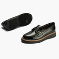 The Pitillos Womens Black Patent Slip On Loafer 10760 features a buckle detail, brown accent stitching on the midsole, and thick black rubber soles. One shoe is upright while the other reveals its ridged sole., 8445191661319, 8445191661326, 8445191661333, 8445191661340, 8445191661357, 51930