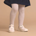 A young child wears a navy blue skirt, white cable-knit tights, and Pretty Brave Miley First Walker Mary Jane T Bar Leather Winter Bloom Pink shoes, standing against a beige background., 9420075361980, 9420075361973, 9420075361966, 9420075361959