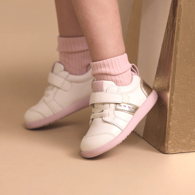 A child wearing light pink socks and Pretty Brave SID Leather Trainer First Walker Off White Stone Pink rests their feet against a gold-painted block on a beige background., 9420075362963, 9420075362956, 9420075362949, 9420075362932