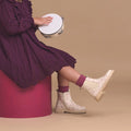 A child in a purple dress and Pretty Brave Girls Hudson Winter Bloom Pink Leather Boots sits on a magenta stool, holding a tambourine against a beige background., 9420075363205, 9420075363199, 9420075363182, 9420075363175, 9420075363168, 9420075363151, 9420075363144, 9420075363137, 9420075363120, 9420075363113