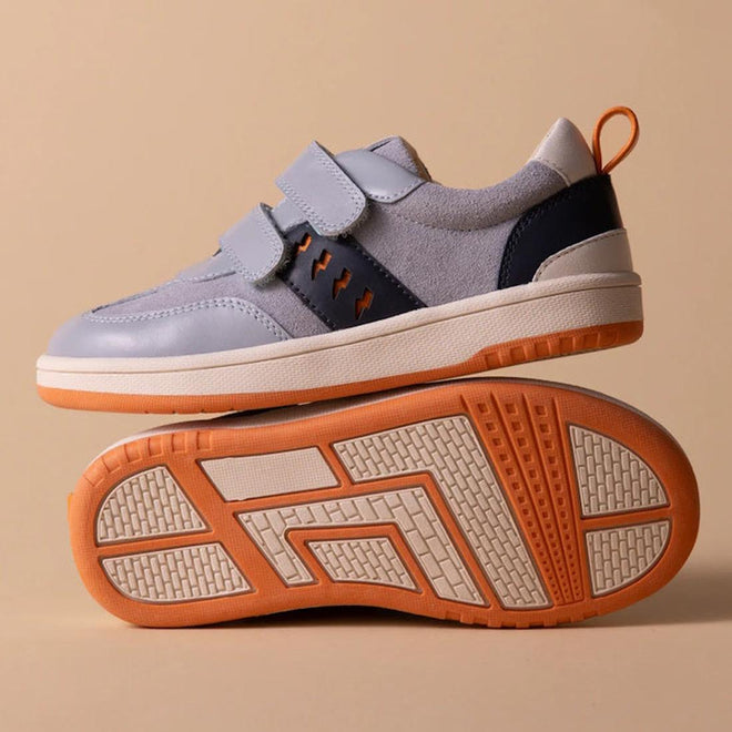 The Pretty Brave River Bolts Leather Trainer Blue Grey is a kids' sporty shoe in light gray and navy with orange accents and white soles. One shoe stands upright, while the other lies on its side to display the textured orange and white sole., 9420075363984, 9420075363977, 9420075363960, 9420075363953, 50510, 50511, 50512, 50513, 50514, 50515, 9420075363984, 9420075363977, 9420075363960, 9420075363953, 9420075363946, 50511, 50512, 50513, 50514, 50515