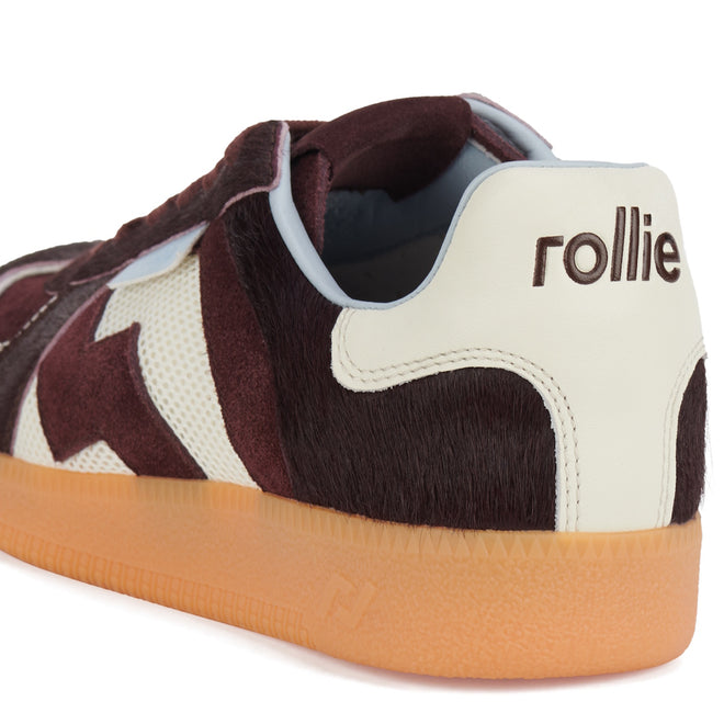 A close-up of the Rollie Womens Pace Dark Cherry Bone Suede Sneaker features a brown and white furry upper, light brown rubber sole, and "rollie" embroidered on the white heel tab., 9339554000315, 9339554000317, 9339554000164, 9339554000056, 9339554000182