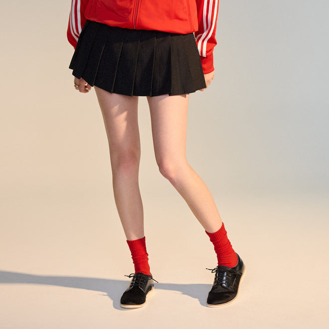 Person wearing a red jacket with white stripes, black pleated skirt, red socks, and Rollie Womens Derby Black Splice Leather Brogue Shoes with an anti-slip rubber outsole, standing against a plain background. Face not visible., 51190, 9339554014920, 9339554054292, 9339554007458, 9339554000329, 9339554389769