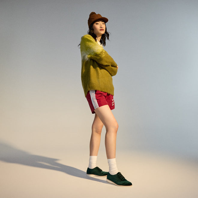A woman stands in a studio wearing a brown knit beanie, SC02101 fuzzy green sweater, red athletic shorts with white stripes, white socks, and Rollie Womens Derby Emerald Velvet Brouge Shoes. She looks confidently at the camera with arms crossed., 9339554068114, 9339554005690, 9339554000077, 9339554000336, 9339554023830