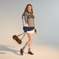 A young woman with long red hair wears a headband, an oversized ICECREAM sweatshirt, pleated white skirt, gray socks, and Rollie Womens Derby Super Soft Dark Cherry Leather Shoes. She holds a brown bag in a minimal, softly lit studio., 9339554034843, 9339554086330, 9339554099231, 9339554070285, 9339554124001, 9339554126029