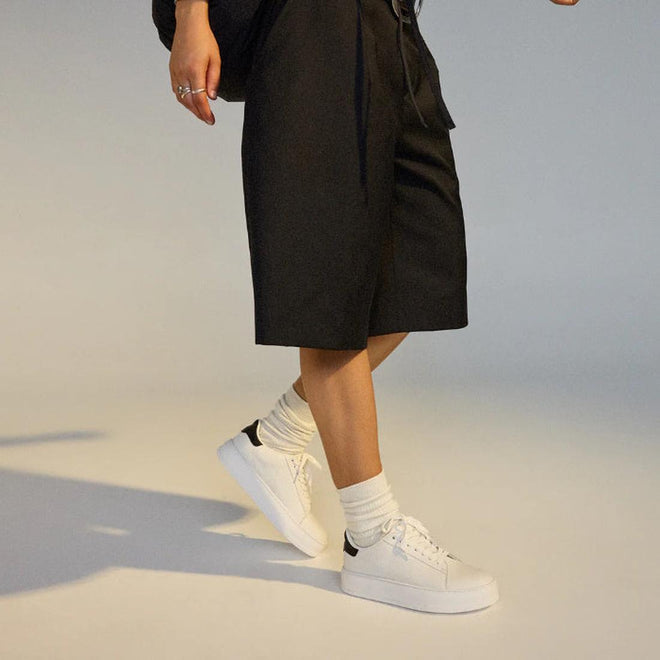 Person in a wlaking poise wearing a black skirt, white rollie club court lace up sneakers, and socks on a neutral background.,
9781760790097,
9781760790103,
9781760790110,
9781760790127,
9781760790134,
9781760790141,