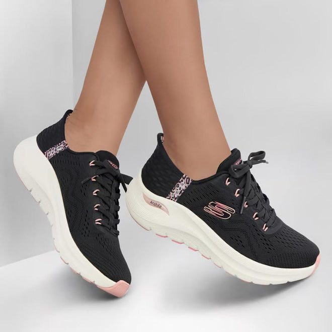 Someone wearing Skechers Arch Fit 2.0 Slip In Spotted Grace Black Multi shoes with white soles and pink accents stands on a white surface, their feet slightly crossed., 199025299961, 48851, 199025299985, 48853, 199025300001, 48855, 199025300025, 48857, 199025300049, 199025300063
