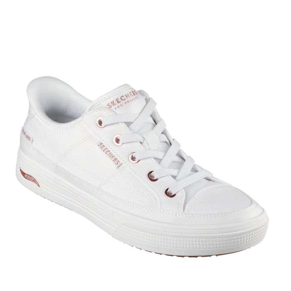 The Skechers Arch Fit-Arcade See Ya There Shoe in white, designed with a wide fit for extra comfort, features slip-in convenience, rose gold accents, white laces, and a thick rubber sole—it is showcased at an angle on a white background.