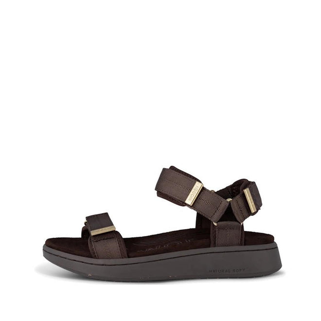 The Woden Line Women's 3 Strap Sandal in Chocolate Brown features adjustable front and ankle straps with metal hardware, detailed stitching, and a thick cushioned sole with Natural Soft technology for comfort.