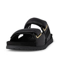The Woden Lisa Women's Leather 2 Strap Sandal in black, featuring wide buckle straps with gold-tone accents and a flat rubber sole, is displayed from the front on a white background.