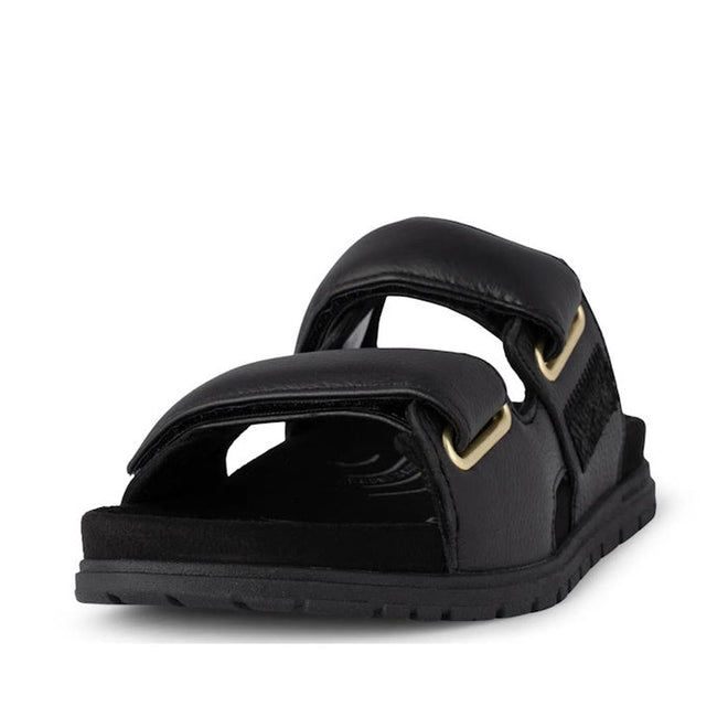 The Woden Lisa Women's Leather 2 Strap Sandal in black, featuring wide buckle straps with gold-tone accents and a flat rubber sole, is displayed from the front on a white background.