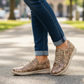 A woman stands on a sunlit park path in rolled-up jeans and Ziera Solar XW Women's Casual Sneaker Zip Chocolate Gold Paisley Brown Leather, highlighting the shoes and her lower legs with trees and blurred buildings in the background., 51033, 4434755528438, 4434755528452, 4434755528476, 4434755528490, 4434755528513, 4434755528520