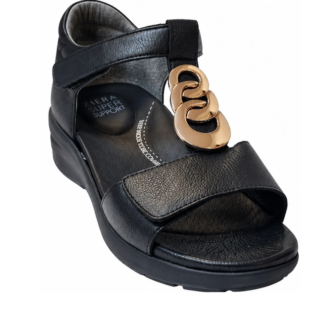 Ziera Nextime Black Leather Womens Sandal with Closed Back XW features a low wedge heel, open toe, and ankle strap. The upper strap is adorned with gold decorative rings, and the insole displays “Ziera Super Support” text. Designed in a wide fit for enhanced comfort, this sandal is orthotic compatible for personalized support.