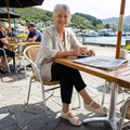 Woman sitting at an outdoor cafe table with a scenic waterfront view. waering Ziera Daffodil Sandals in ALmond Off white closed back sanalds with open toes, cut outs on the leather and velcro fastening over the toes., 49093, 49094, 9351017754167, 9351017754174, 9351017754181, 9351017754198, 49099